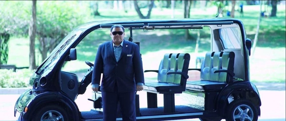 Iso ja leveä henkivartijan näköinen kaveri, pienen pidennetyn golf-kärryn edessä.