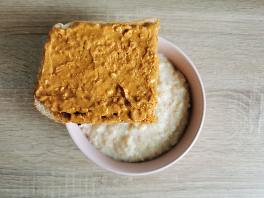 Миска овсянки и сверху тост, намазанный арахисовой пастой с кусочками орехов.
