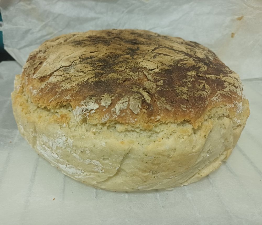 Foto de un pan casero, con la parte de abajo menos tostada que la parte de arriba. Está sobre un papel de horno.