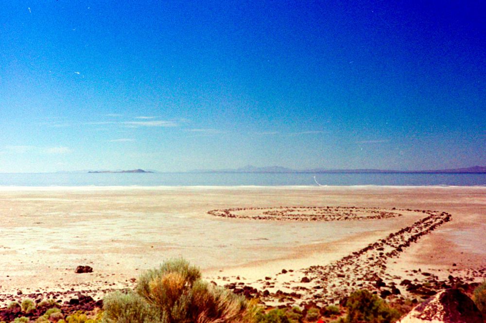 Color photo showing the Spiral Jetty land art created by Robert Smithson along the shores of the Great Salt Lake in Utah. It uses basalt rock that was moved from the hill that is directly behind where I am taking this photo.

When originally created, the Jetty was in the water. During the late 90s and early 00s, the water covered the Jetty and people were known to kayak overtop of it. Today, mostly due to significant urban development, the lake is now nearly a mile from the Jetty.