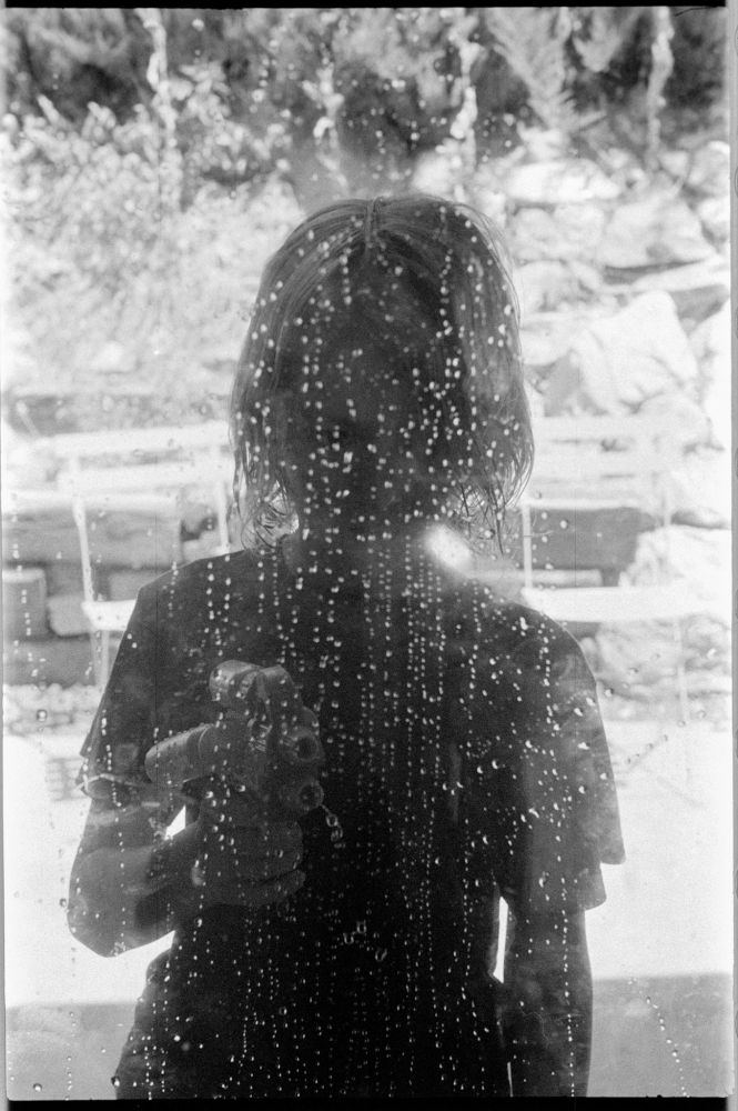 The bright background framed the ominous silhouette of the boy. Crystal like spots like a beaded curtain on the window pane were testament to the close call I had with becoming drenched from a water pistol onslaught.