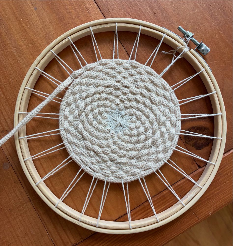 A round warp of natural colored linen thread with natural colored, flat cord woven in the round.