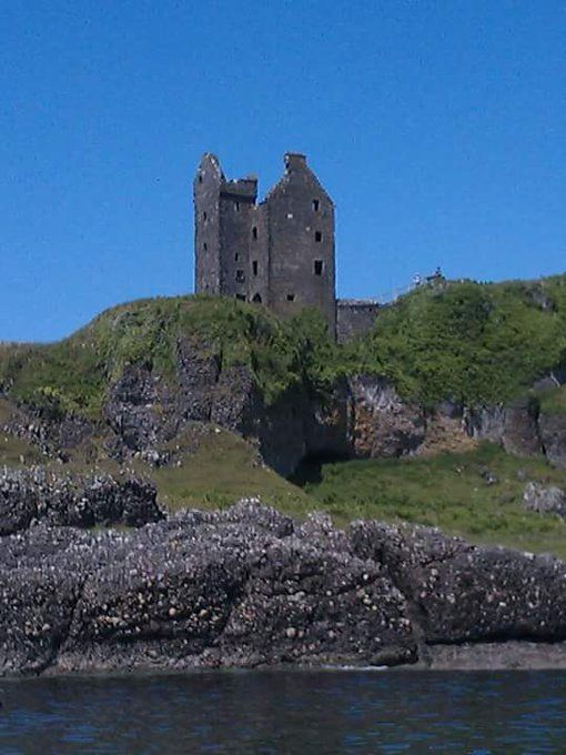 A derelict castle stands high above a sea cliff with pure blue sky above. 