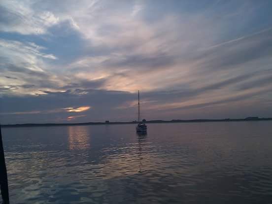 Sailing boat at anchor with pink, grey and blue colours of sunset over the very low-lying island of Tiree, Inner Hebrides. Scotland. 