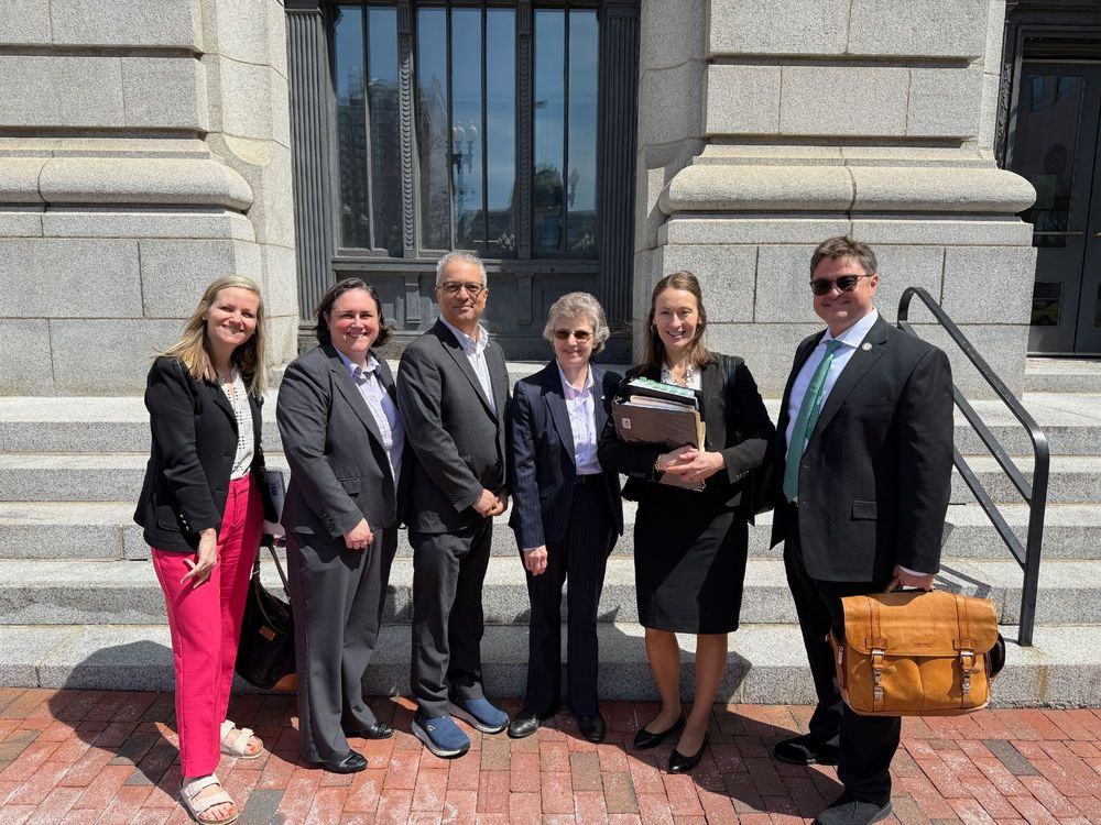 Picture of Ed Garcia of Cranston Public Library, Rhode Island State Librarian Karen Mellor, and other advocates standing in front of a federal courthouse in Providence with attorneys representing the Rhode Island Attorney General.