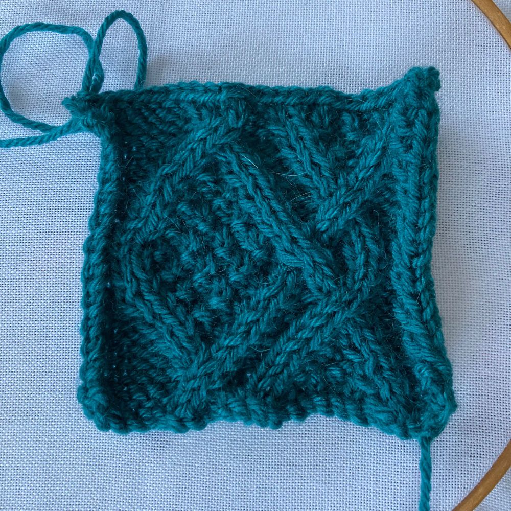 Teal green knitted square with bold cable design. 