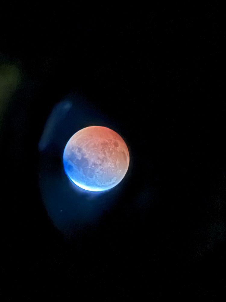 The moon viewed through a telescope, awash in reds and blues during a lunar eclipse.