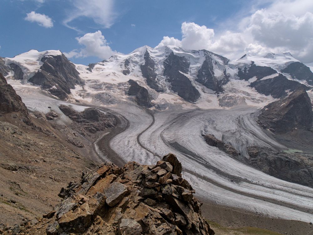 Der Persgletscher in Gruabünden, im Hintergrund der Piz Palü. Der Gletscherabgang geht nach rechts aus dem Bild raus ins Val Bernina. Im Vordergrund ist ein Stein zu sehen auf dem Hang des Mont Pers.