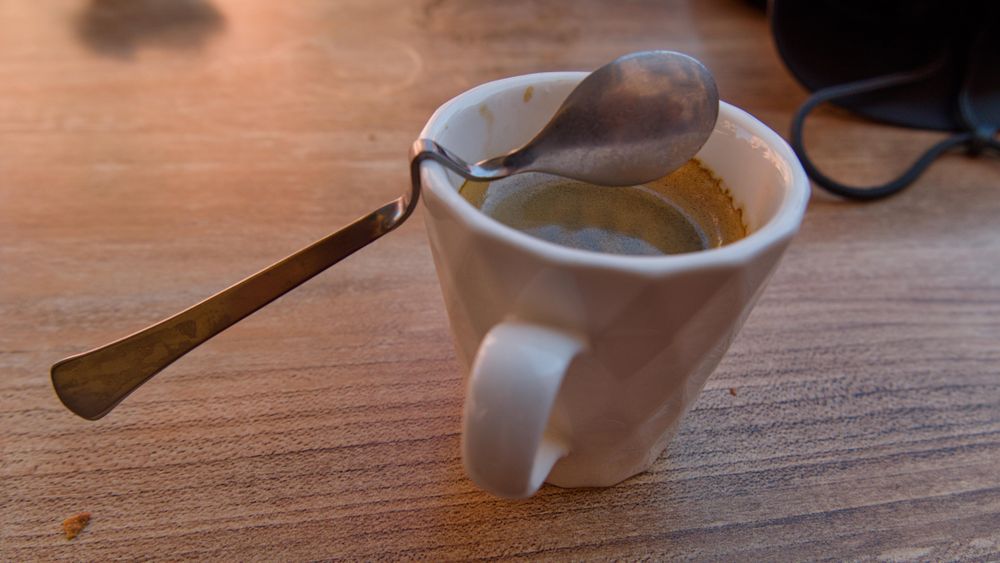 A spoon balanced on the edge of a full espresso cup.