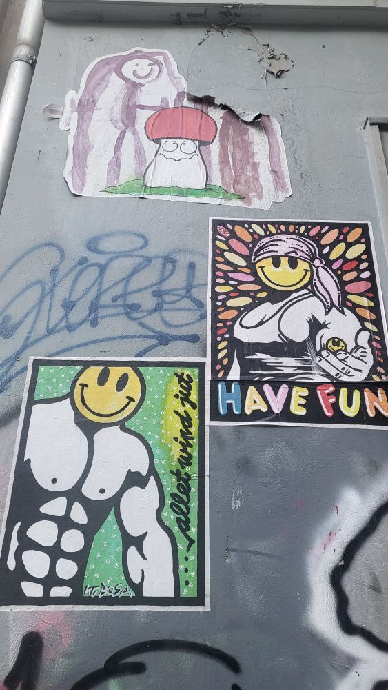 A collection of street art pieces including a cute mushroom character with glasses, and two smiley face sticker artworks with "HAVE FUN" text, combining black and white figures with colorful backgrounds.