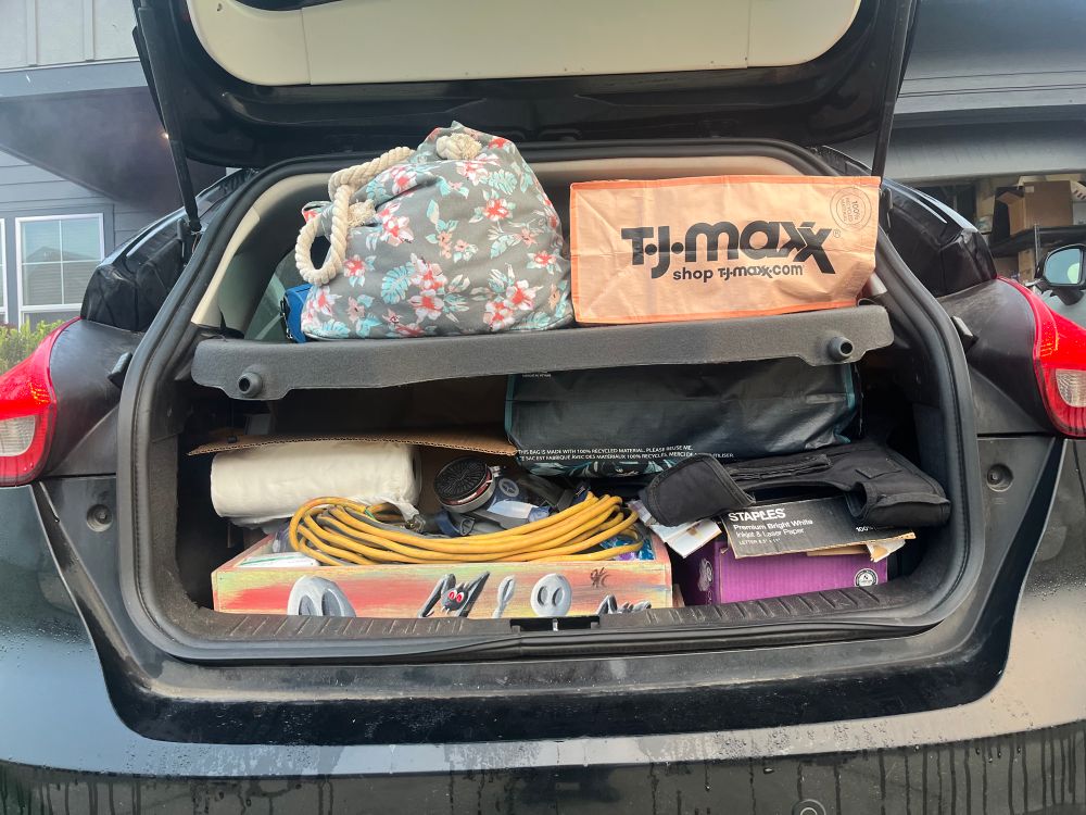 Image shows the open back of a hatchback crammed, full of shoes, boots and winter clothing along with harm reduction supplies