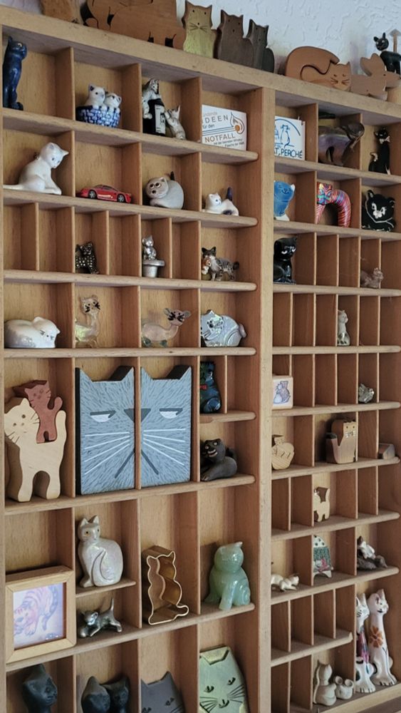 Hochformat. Ein alter Setzkasten bestückt mit einer Katzensammlung aus Holz, Keramik, Metall und mehr.