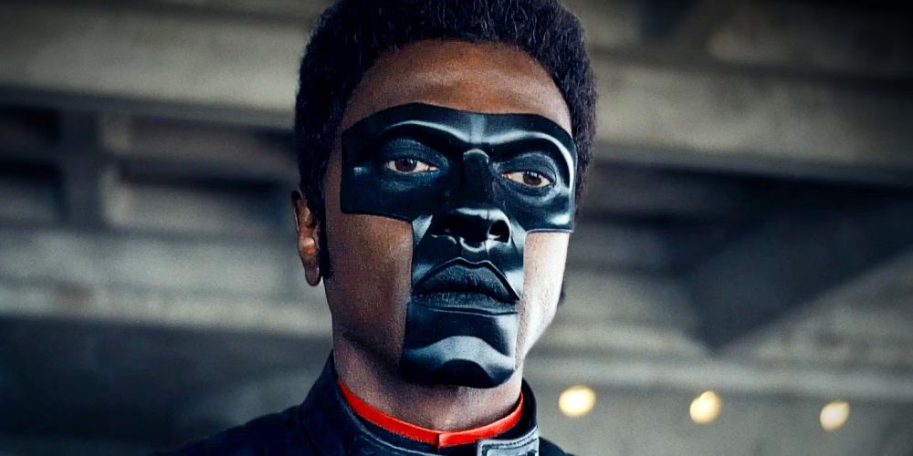ator Edi Gathegi em cena de superman (2025). homem negro com mascara em formato de "T" preta