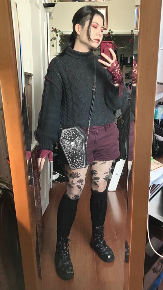 Vinnie in a dark grey cable knit jumper with maroon thread detail, maroon lace gloves, maroon shorts, stockings with black lace roses, leg warmers with black lace ribbon detail, and black boots with flowers and plants on them. 