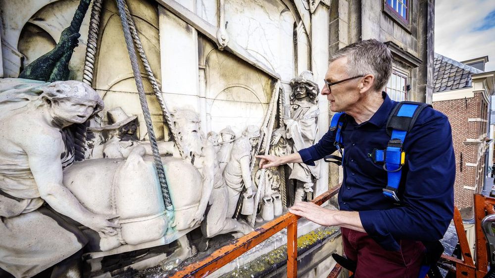 Met schokkende bewegingen gaat de hoogwerker voor de Waag in Leiden omhoog. De specialisten in het bakje zien even later iets bijzonders van dichtbij: het marmeren basreliëf van Rombout Verhulst en in detail het verval van dit kunstwerk.