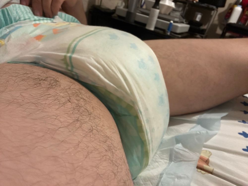 Photo of me wearing a very soggy TryAgains diaper, laying on a puppy pad placed on my bed. View from the side to show off the sog~