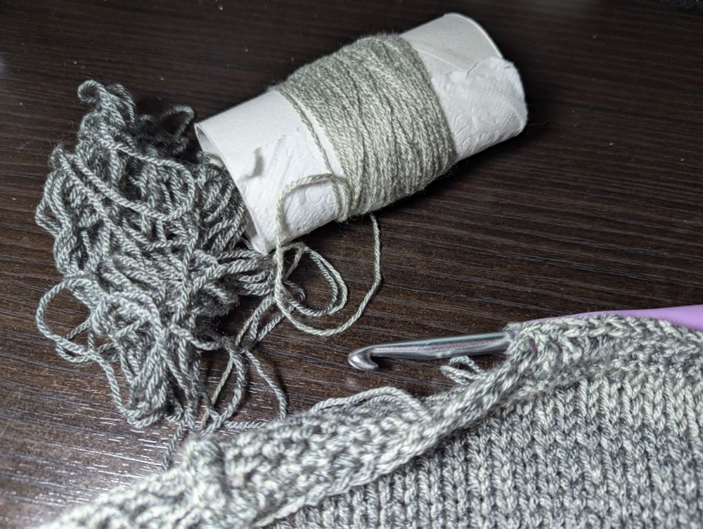 Edge of a knitted panel with an incomplete crochet border. A small amount of unused yarn. 