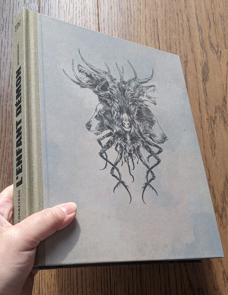 Un livre épais, à la couverture toilée, dans les tons kaki et gris, avec un effet un peu sali. Un grand motif sur la couverture, à l'encre noire : des têtes d'animaux entremêlées, avec des cornes de bouc et de cerf en haut, et des pattes d'insecte en bas.