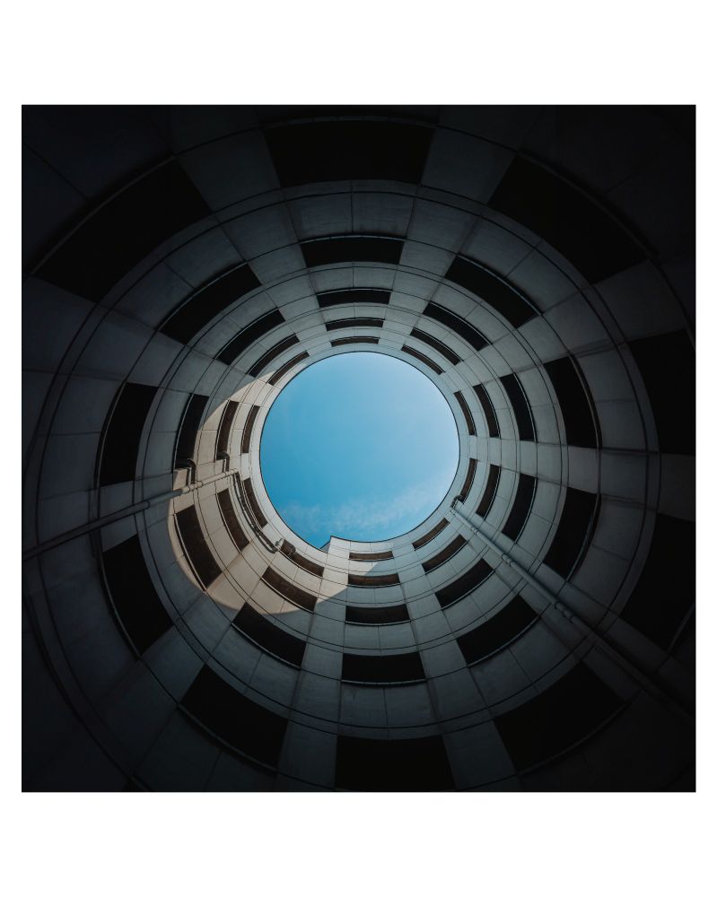 A view up the centre of a roundabout in a parking garage, looking straight up at the sky.