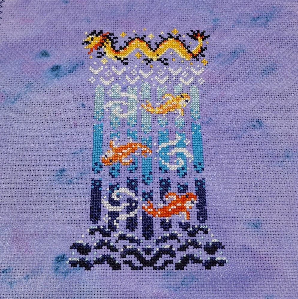 A detailed cross-stitch on a tie-dye style purple background depicts a stylized golden dragon at the top, followed by three orange koi fish swimming downwards through a waterfall in shades of blue, white, and dark purple.