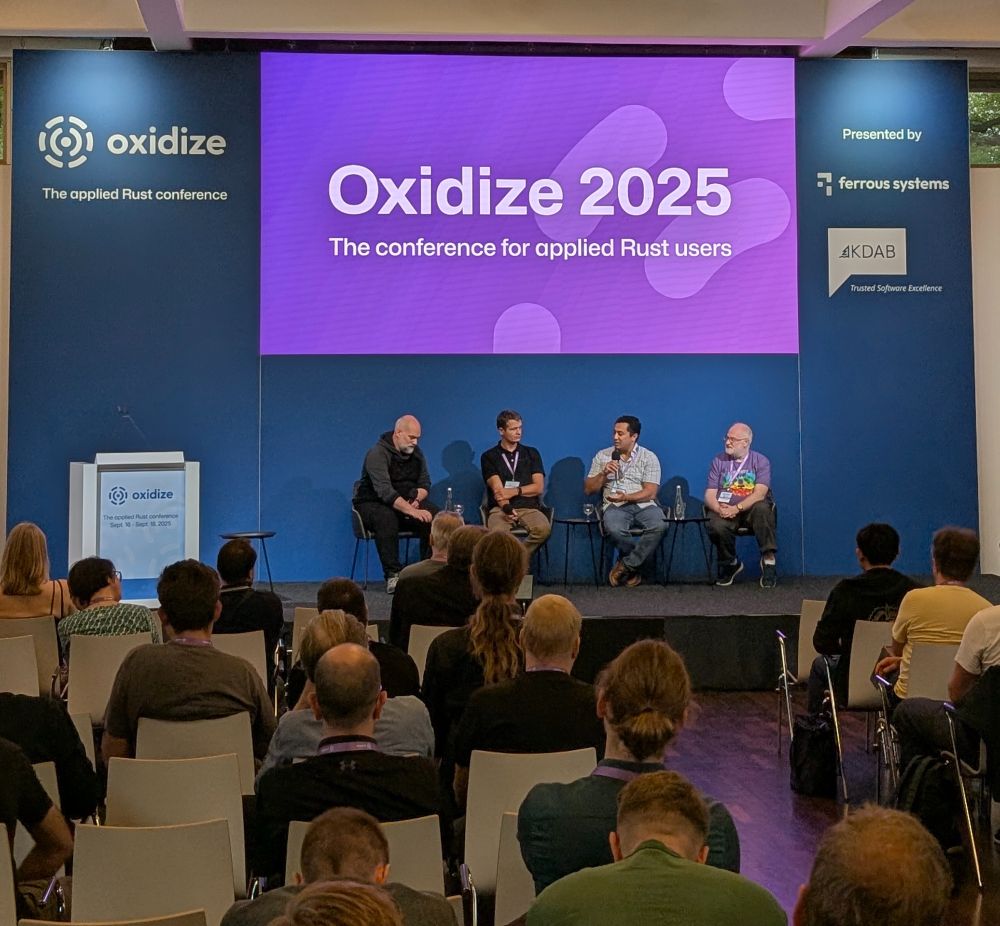An image showing the cast of the panel “Rust in Safety Critical” at Oxidize 2025. Showing from left to right Florian Gilcher (Ferrous Systems), Jonas Wolf (Vector), Rolland Dudemaine (TrustInSoft), Daniel Silverstone (Codethink).