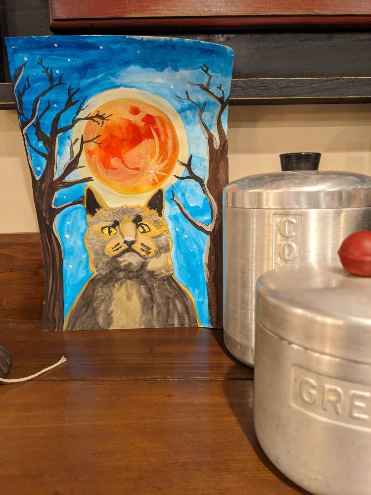 The cat painting I did, sitting against the wall on a cabinet with antique metal containers next to it. 
