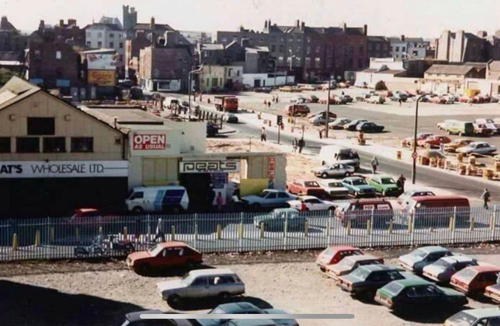 Parnell St in Dublin in 1985. There is a large building with a sign saying “Peats Wholesale”. There are several derelict sites being used as surface car parking.