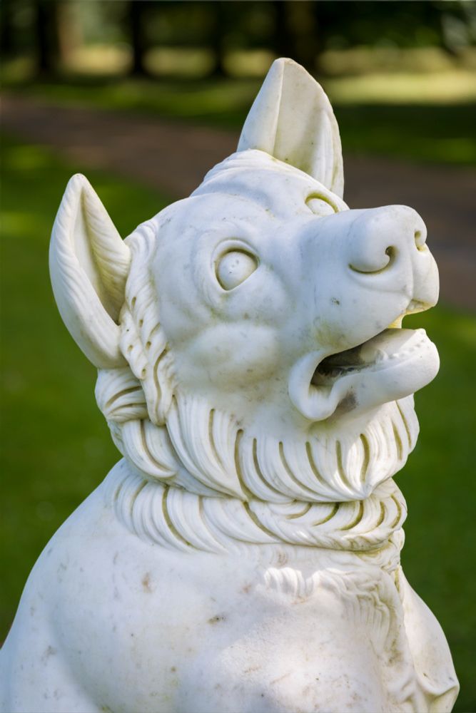 A white marble statue of a pointy-eared dog, looking up at the sky in horror and despair