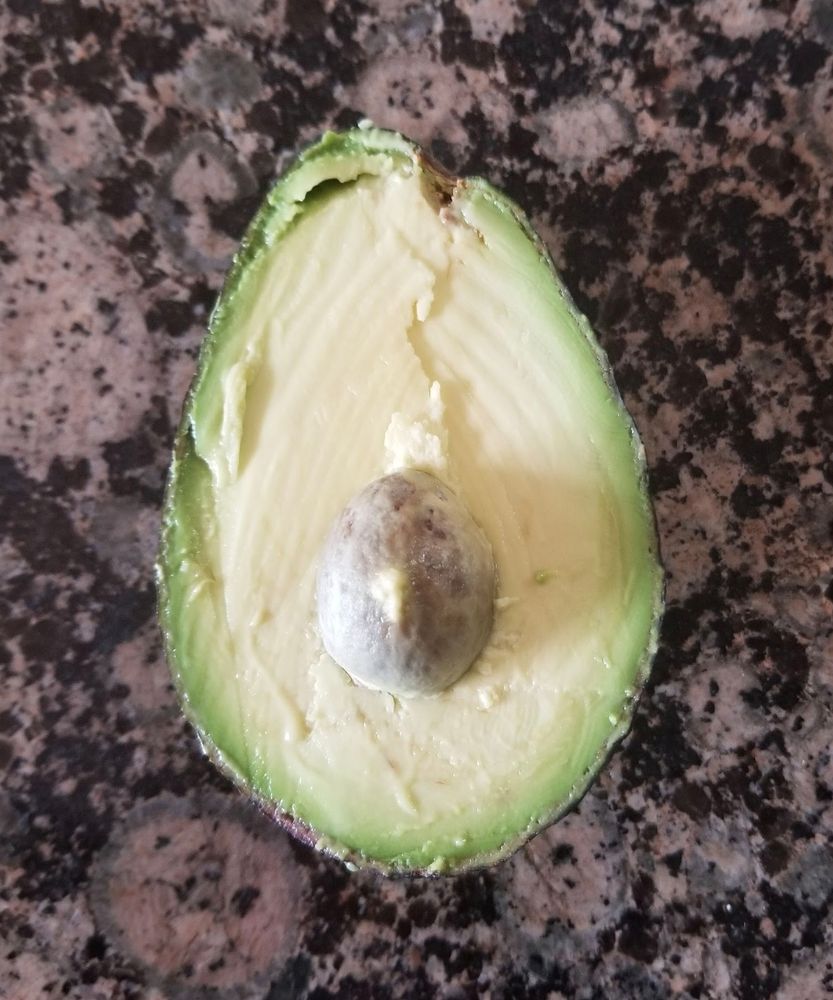 Picture of half of a perfect avocado on a black & pink countertop. Captured in the 5 minutes between rock hard & rotten, it is perfectly ripe and has a very small seed. 