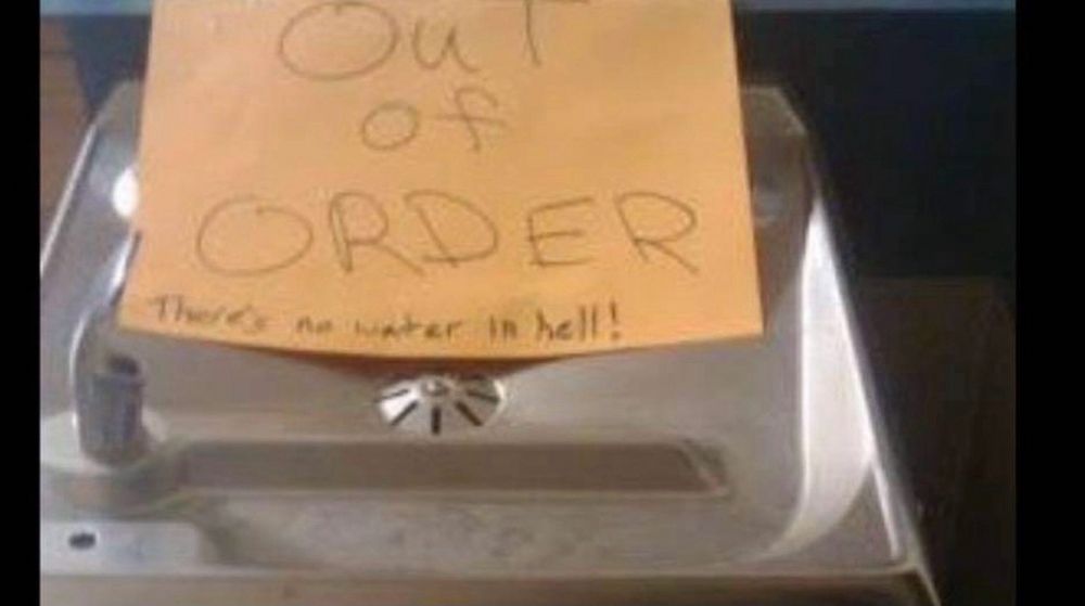 A yellow post it on a water fountain reading “Out of Order” and then in smaller letters beneath, “there’s no water in hell!”