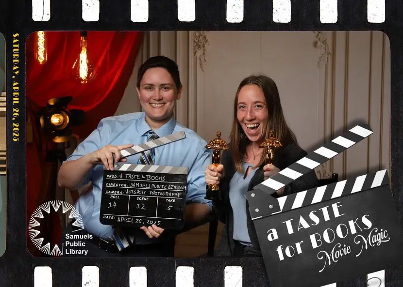 A professional photo of two people, one with short brown hair, a blue shirt and blue and silver tie. They are holding a directors clack board. The other has long brown hair and is holding two mini Oscar statues. In the corner is a superimposed directors clack board with “A Taste for Books: Movie Magic” written on it. 
