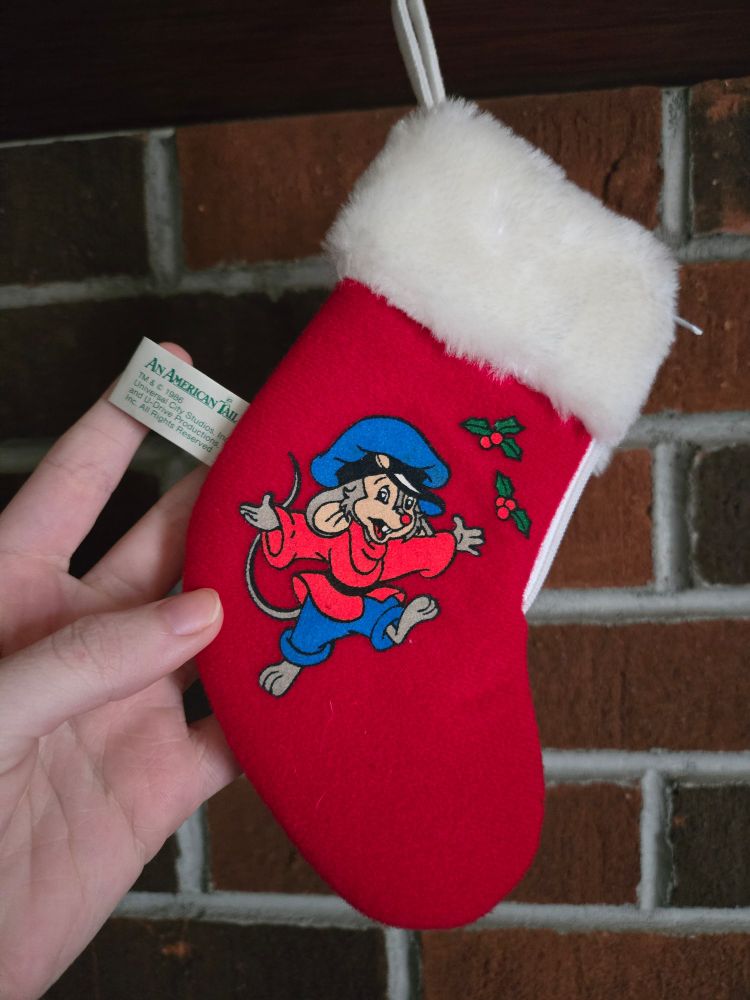 a mini stocking, red with white trim, featuring a picture of Fievel from An Americal Tail (1986) and mistletoe. It is from a McDonald's and Sear's christmas ornament collectible line.