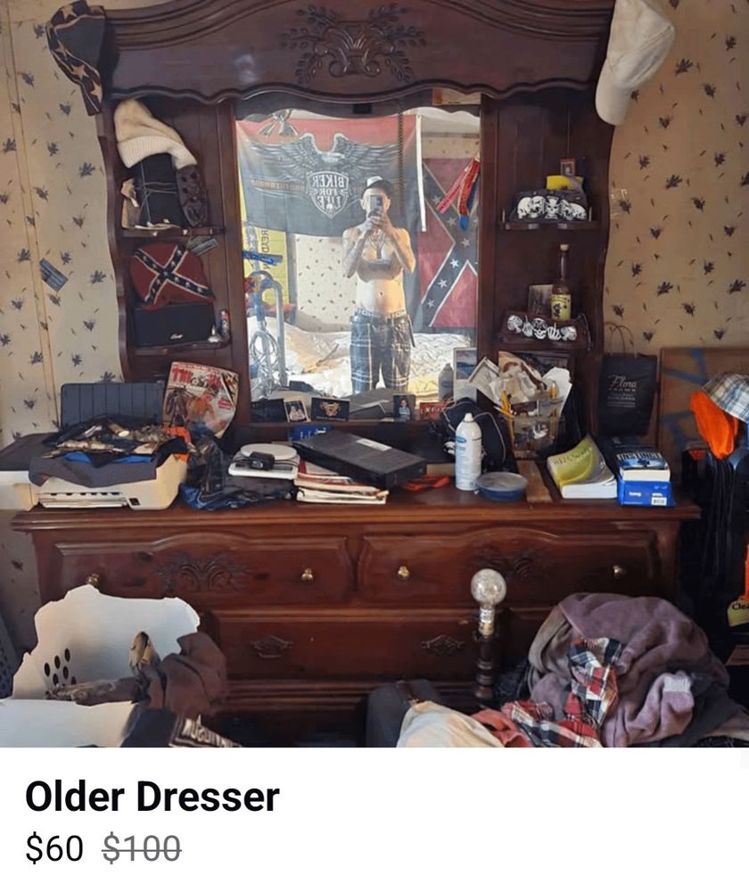 A Craigslist or Marketplace online ad posting featuring a shirtless redneck standing in front of an old dresser with a shelf and mirror topper. His reflection in the mirror as he snaps a pic is prominent. The dresser is covered with trashy clutter and even trashier rebel flags. The caption reads “old dresser” and the original price of $100 is crossed out and replaced by the new price of $60. 