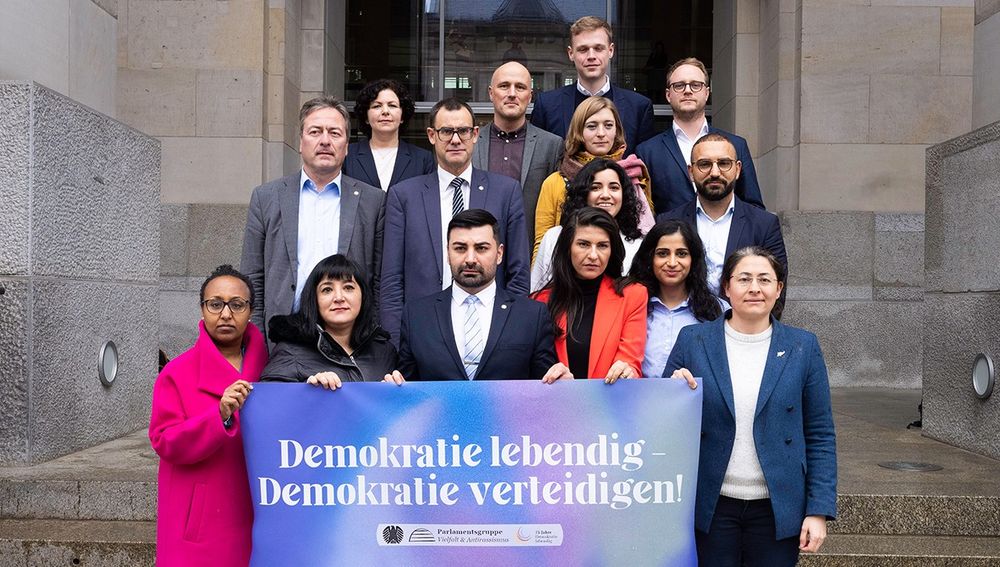 Auf dem Foto ist die interfraktionelle Parlamentsgruppe Vielfalt & Antirassismus zu sehen, die auf den Stufen vor dem Reichstag steht und ein Banner hält auf dem steht: Demokratie leben - Demokratie verteidigen!