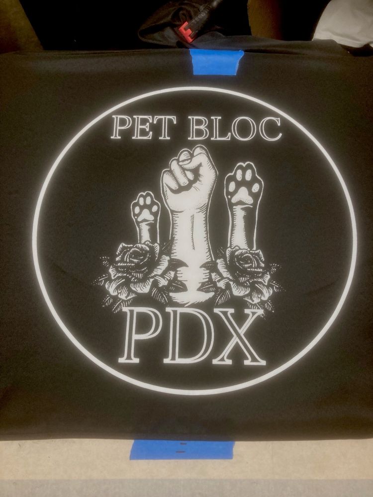 black tablecloth with large white circular print featuring a raised human fist along with upraised dog and cat paws and a couple roses.  text states "Pet Bloc PDX"