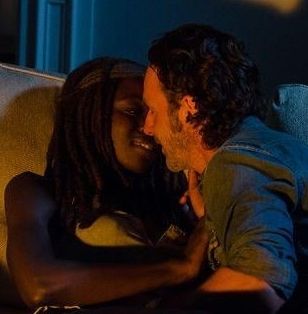 Rick and Michonne Grimes pictured. Michonne smiling with eyes heavy lidded and Rick's eyes are closed as he goes in for another kiss. 
