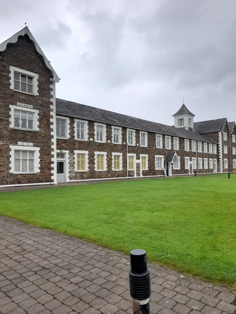 A long two storey brick building with 3 story blocks either ends. Green grass in front. 