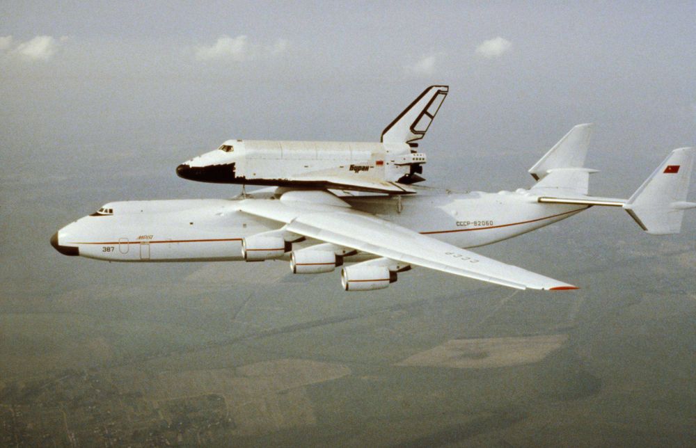 Aerial view of a USSR Buran shuttle being carried on the back of an Antonov An-225 plane.