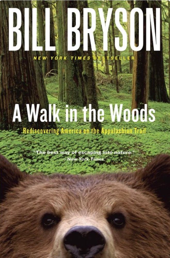 The cover of Bill Bryson’s A Walk in the Woods. The cover depicts a close up of a bear staring at the camera with a forest in the background. 