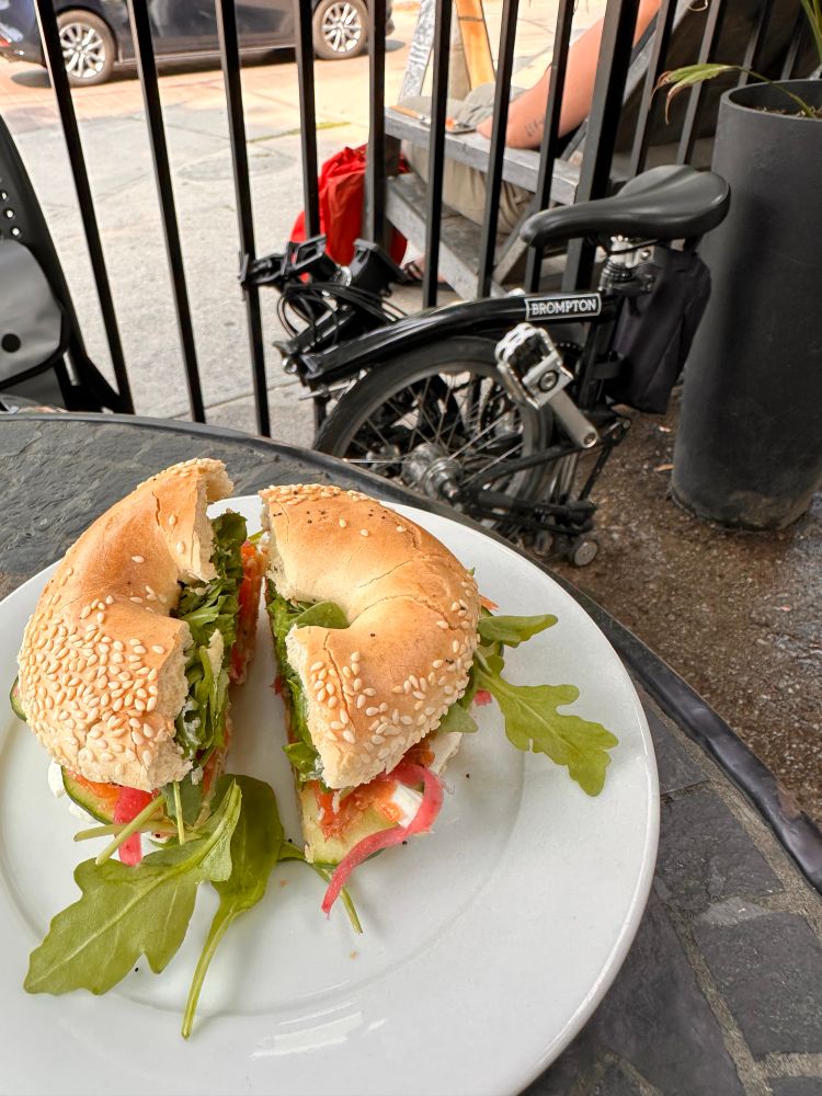 Foreground is a bagel sandwich, below is a folded Brompton Bicycle. 