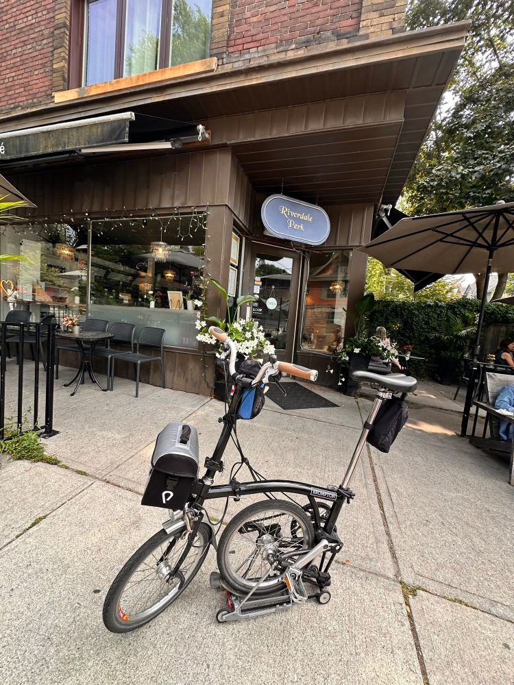 Brompton bicycle 1/3 folded in front of a Cafe. 