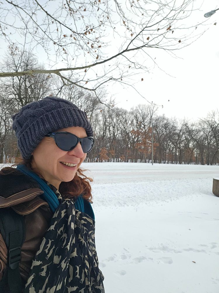 A woman is winter clothes and stocking cap outside in the snow.