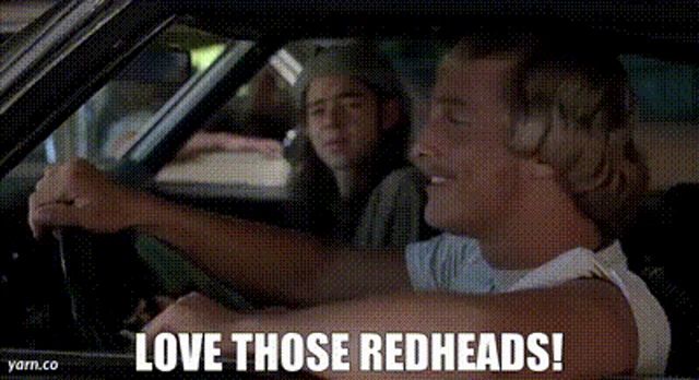 a man is driving a car with the words `` love those redheads ! '' written on the screen .