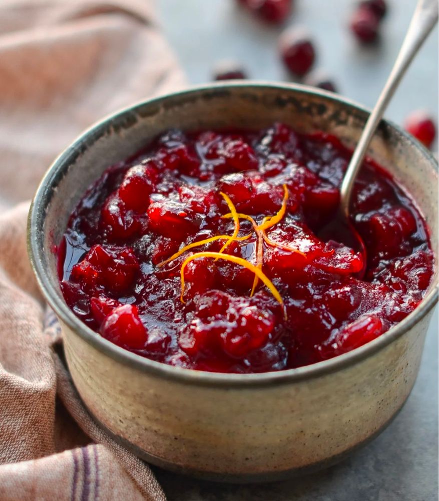 Handmade ceramic bowl with rustic tones, filled with homemade cranberry sauce, garnished with orange zest. 