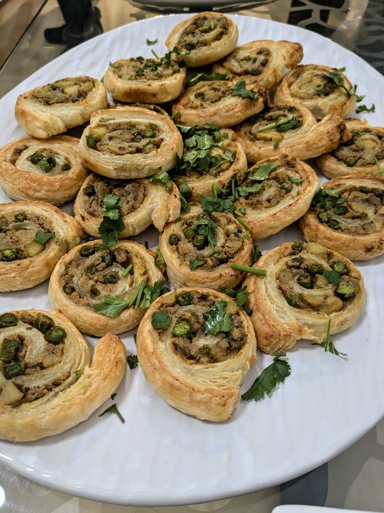 Puff pastry pinwheel samosas, on a textured white oval platter, sprinkled with cilantro. 