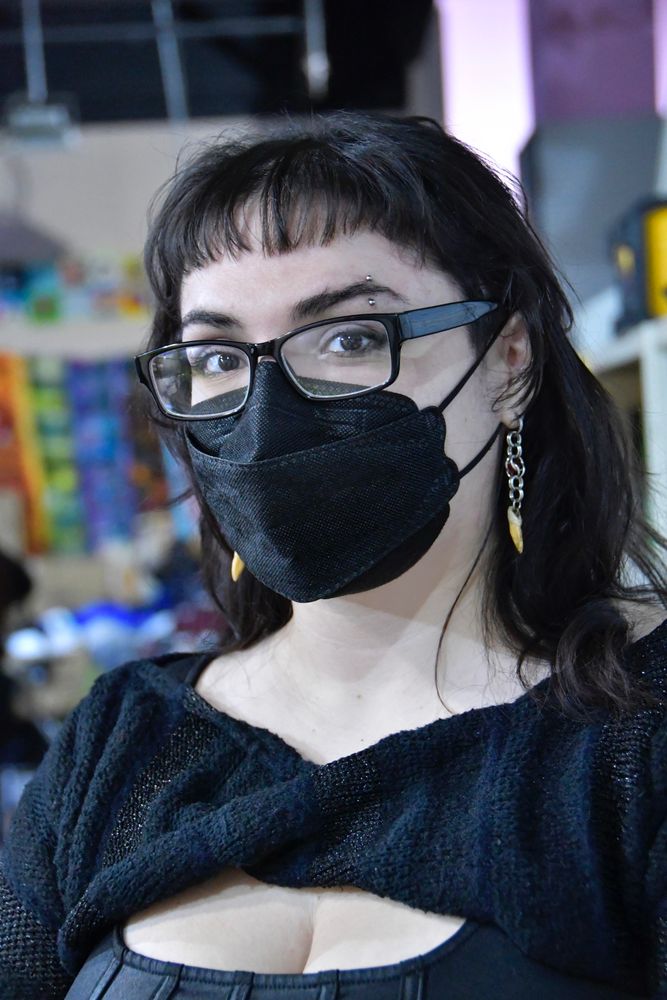 Elena, wearing black framed glasses, black KF94 respirator and a black top, posed for Julie Lam to support the documentary project Julie created for MaskTogetherAmerica