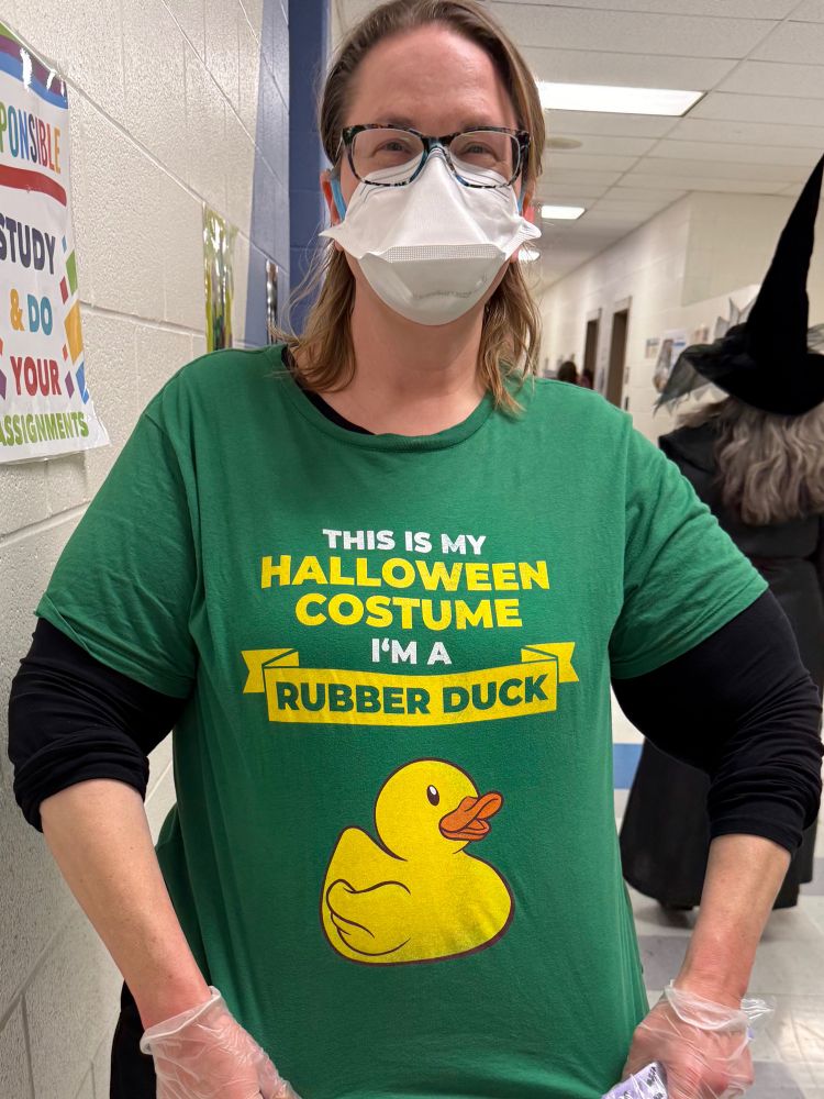 Norah Mason is wearing a duckbill N95, glasses and a green T-shirt that has an illustration of a rubber ducky and white and yellow text that says, “This is my Halloween Costume. I’m a Rubber Duck.”