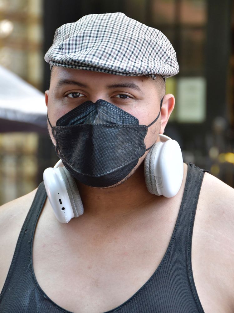 A volunteer, wearing a black KF94 respirator, a vintage wool tweed cap, a white headset, a sleeveless top, posed for Julie Lam to support MaskTogetherAmerica