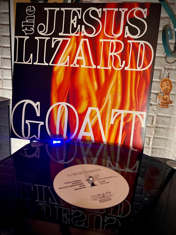 The Jesus Lizard - Goat (1991) spins on a turntable. Its cover art, by bassist David Wm. Sims, at first glance resembles a flame, but is actually a topless woman with a close-up image of nails projected onto her body.