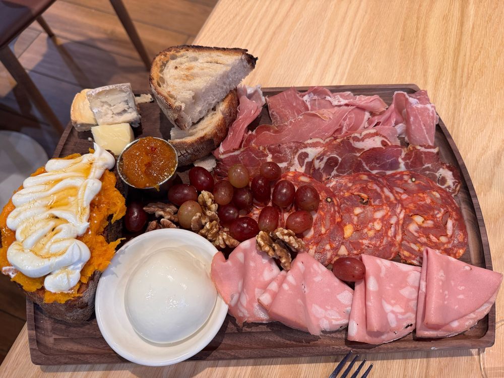 Boston charcuterie tray with various meats, cheeses, baked sweet potato with something creamy on top, walnuts and fruit. 